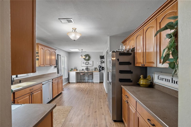 kitchen with visible vents, light wood-style flooring, appliances with stainless steel finishes, decorative light fixtures, and a sink