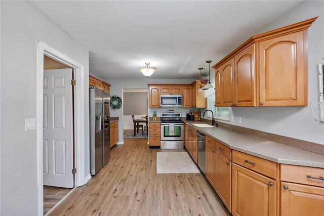 kitchen with pendant lighting, light wood finished floors, light countertops, appliances with stainless steel finishes, and a sink