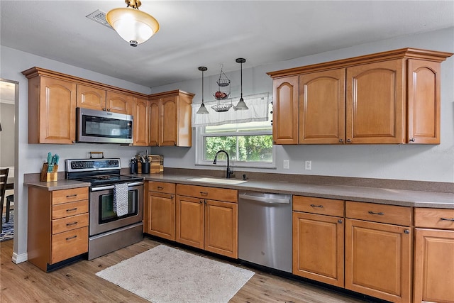 kitchen featuring a sink, hanging light fixtures, appliances with stainless steel finishes, light wood-type flooring, and brown cabinetry