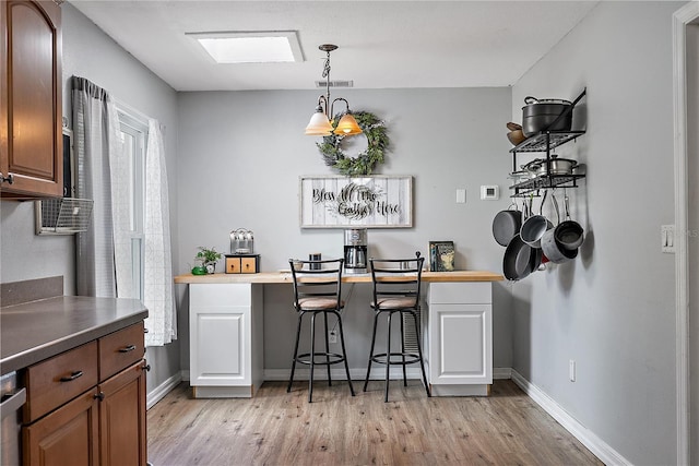 kitchen with pendant lighting, dark countertops, visible vents, light wood-style floors, and baseboards