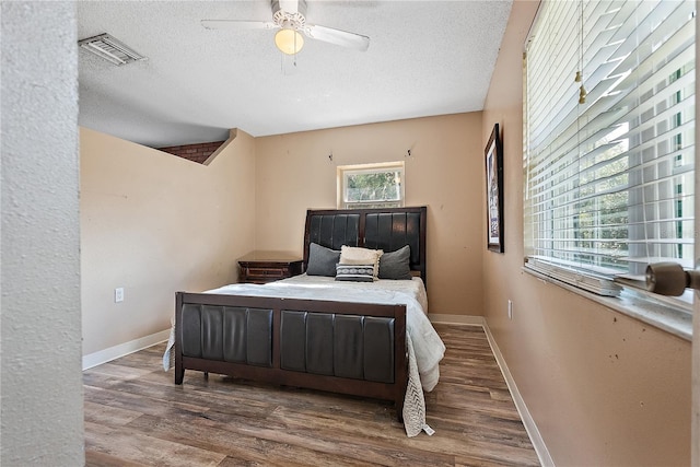 bedroom with visible vents, a textured ceiling, baseboards, and wood finished floors