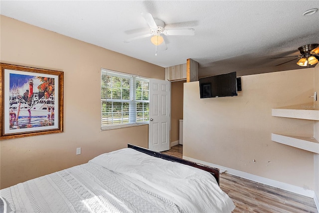 bedroom featuring light wood-style flooring, baseboards, ceiling fan, and a textured ceiling