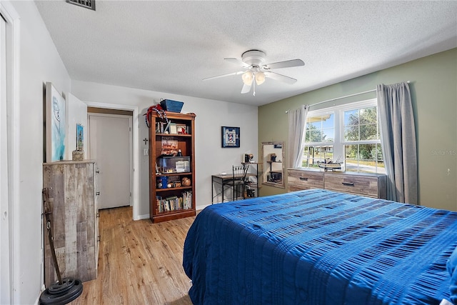 bedroom featuring light wood finished floors, visible vents, baseboards, ceiling fan, and a textured ceiling