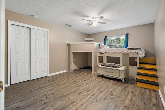 bedroom with a textured ceiling, wood finished floors, visible vents, baseboards, and a ceiling fan