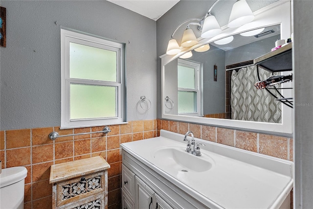 bathroom featuring toilet, wainscoting, tile walls, and vanity