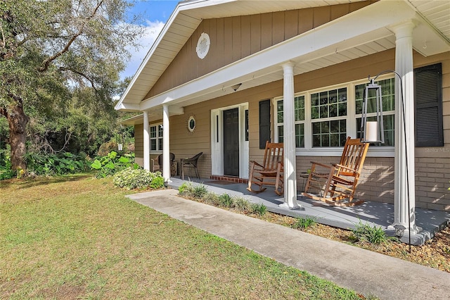 doorway to property with covered porch, a yard, and brick siding