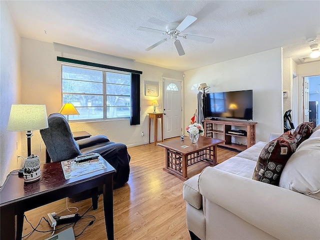 living room with ceiling fan, a textured ceiling, and light wood-type flooring