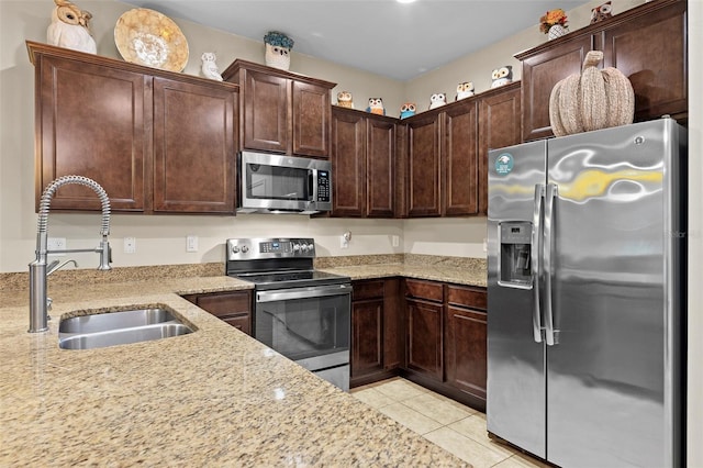 kitchen with light stone countertops, dark brown cabinets, stainless steel appliances, sink, and light tile patterned floors