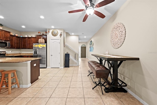 kitchen with a kitchen bar, appliances with stainless steel finishes, light stone countertops, ceiling fan, and light tile patterned flooring