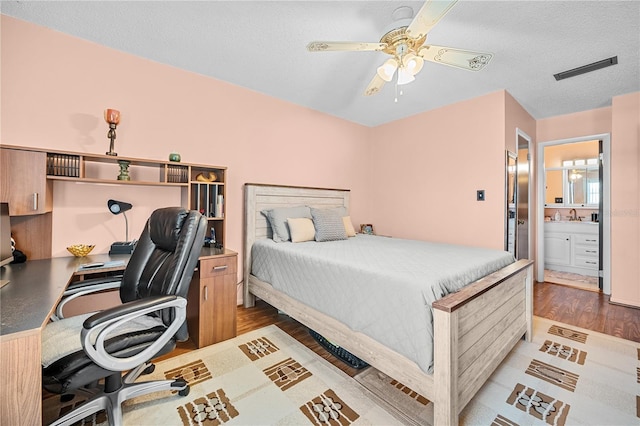 bedroom featuring hardwood / wood-style floors, ceiling fan, a textured ceiling, and ensuite bath