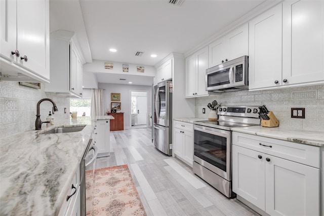 kitchen with white cabinets, appliances with stainless steel finishes, light stone countertops, and sink