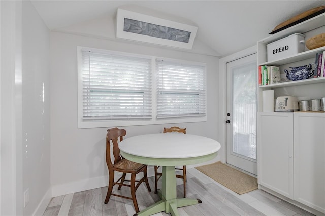 dining area with a healthy amount of sunlight, light wood-type flooring, and vaulted ceiling