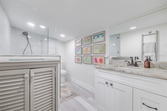 bathroom with tiled shower, hardwood / wood-style floors, vanity, and toilet