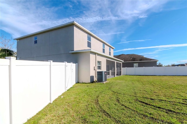 rear view of house with central air condition unit, a lawn, and a sunroom