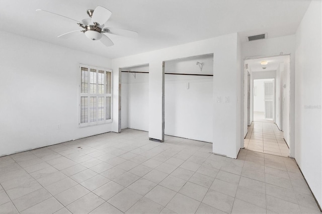 unfurnished bedroom with ceiling fan, light tile patterned floors, and multiple closets