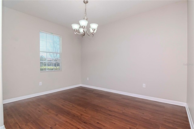 empty room with dark wood-type flooring and an inviting chandelier