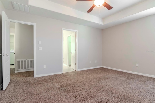 carpeted spare room with ceiling fan and a raised ceiling