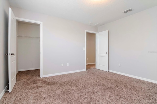 unfurnished bedroom featuring carpet, a walk in closet, and a closet