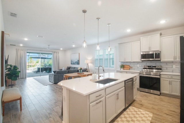 kitchen with sink, hanging light fixtures, an island with sink, light hardwood / wood-style floors, and stainless steel appliances