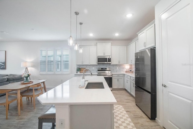 kitchen with sink, decorative light fixtures, a kitchen island with sink, white cabinets, and appliances with stainless steel finishes