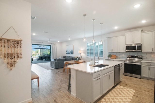 kitchen with a center island with sink, hanging light fixtures, sink, light hardwood / wood-style flooring, and appliances with stainless steel finishes