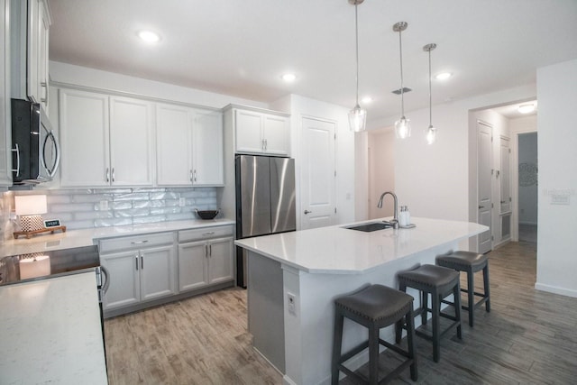 kitchen with appliances with stainless steel finishes, tasteful backsplash, sink, a center island with sink, and hanging light fixtures