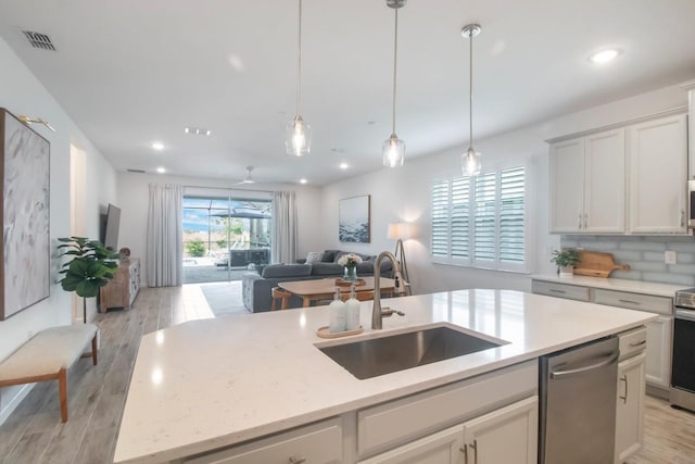 kitchen with sink, stainless steel appliances, light hardwood / wood-style floors, decorative light fixtures, and a center island with sink