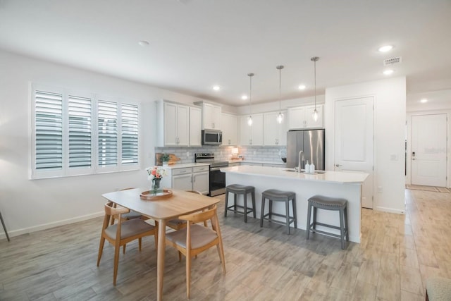 kitchen with appliances with stainless steel finishes, sink, white cabinetry, hanging light fixtures, and an island with sink