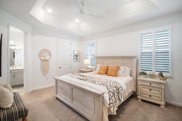 carpeted bedroom with ceiling fan, a raised ceiling, and connected bathroom