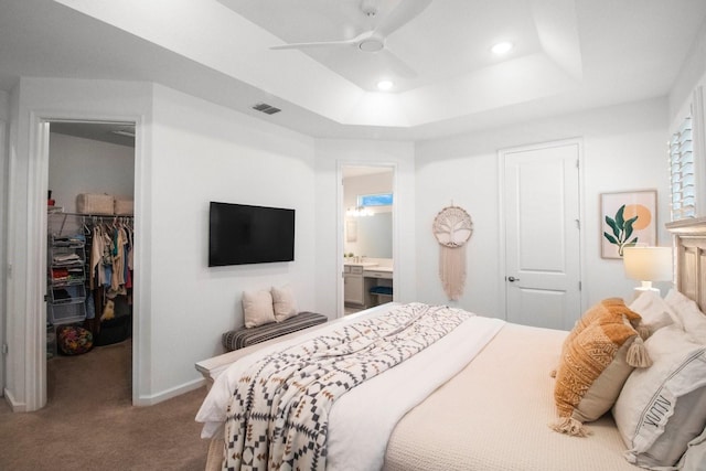 carpeted bedroom with ensuite bath, ceiling fan, a spacious closet, a tray ceiling, and a closet