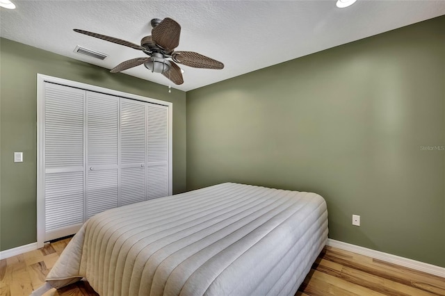 bedroom featuring a textured ceiling, a closet, light hardwood / wood-style flooring, and ceiling fan