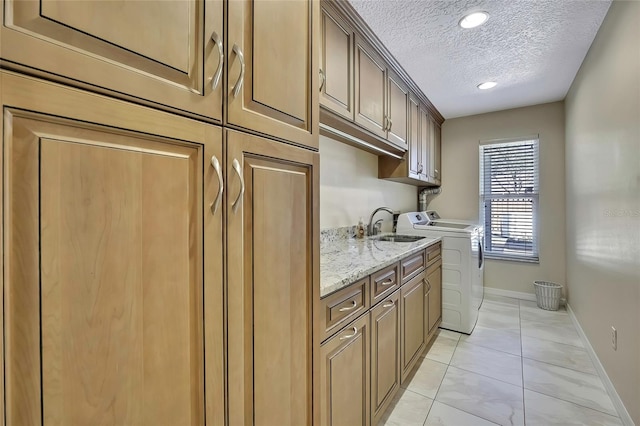 kitchen featuring light stone counters, washer and dryer, sink, and a textured ceiling