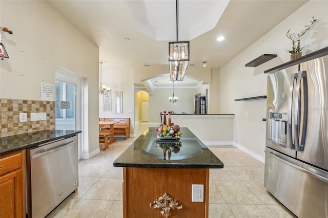 kitchen featuring dark stone counters, light tile patterned floors, a tray ceiling, decorative light fixtures, and stainless steel appliances