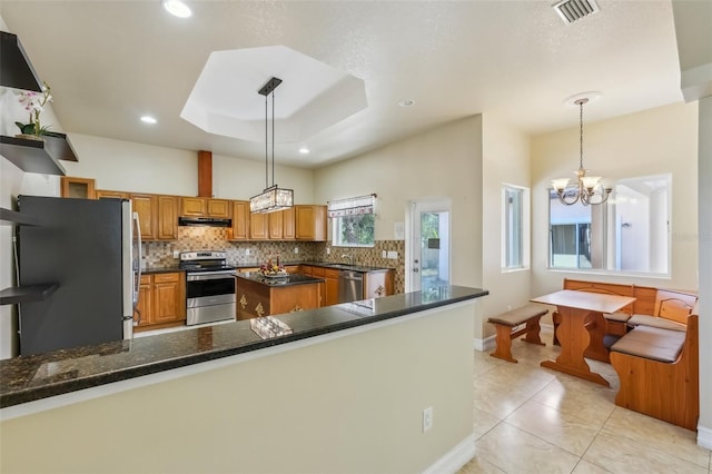 kitchen with a notable chandelier, pendant lighting, a tray ceiling, light tile patterned flooring, and appliances with stainless steel finishes