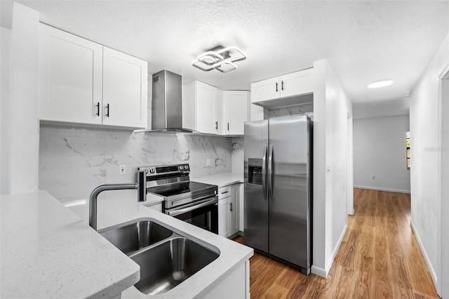 kitchen featuring appliances with stainless steel finishes, tasteful backsplash, wall chimney exhaust hood, light hardwood / wood-style floors, and white cabinetry