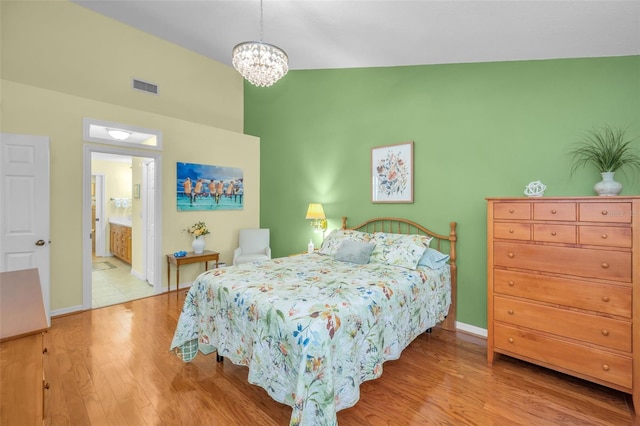 bedroom featuring connected bathroom, light hardwood / wood-style flooring, and an inviting chandelier