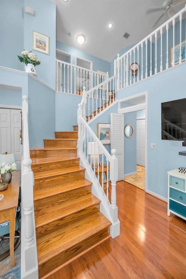 stairway featuring wood-type flooring, ceiling fan, and a high ceiling