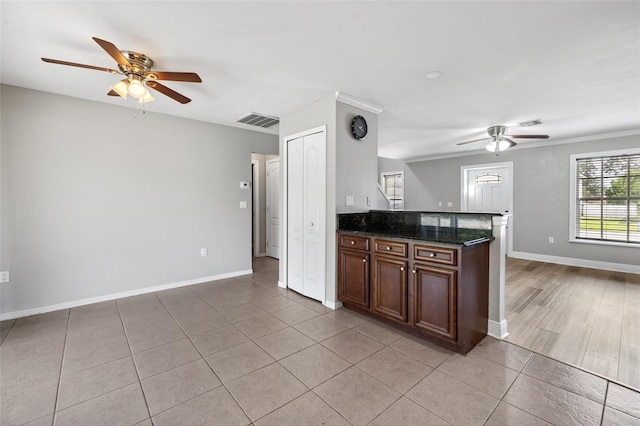 kitchen featuring ceiling fan, light tile patterned flooring, dark stone counters, and ornamental molding