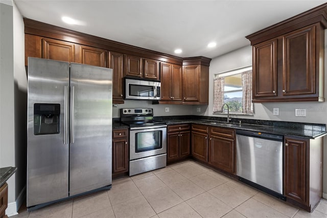 kitchen with dark brown cabinetry, stainless steel appliances, sink, light tile patterned floors, and dark stone countertops