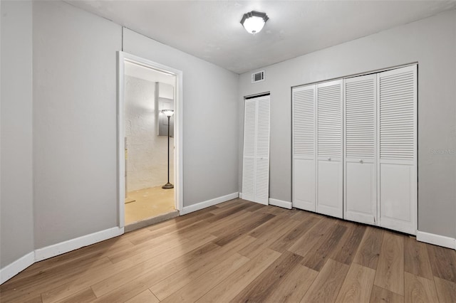 unfurnished bedroom featuring ensuite bathroom, light hardwood / wood-style floors, and two closets