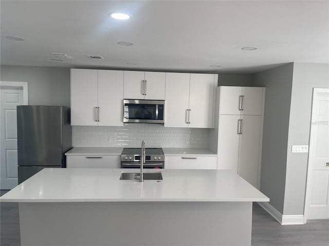 kitchen featuring backsplash, light stone counters, stainless steel appliances, wood-type flooring, and white cabinetry