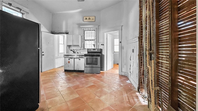 kitchen with white cabinets, light tile patterned floors, black refrigerator, and stainless steel range with electric cooktop