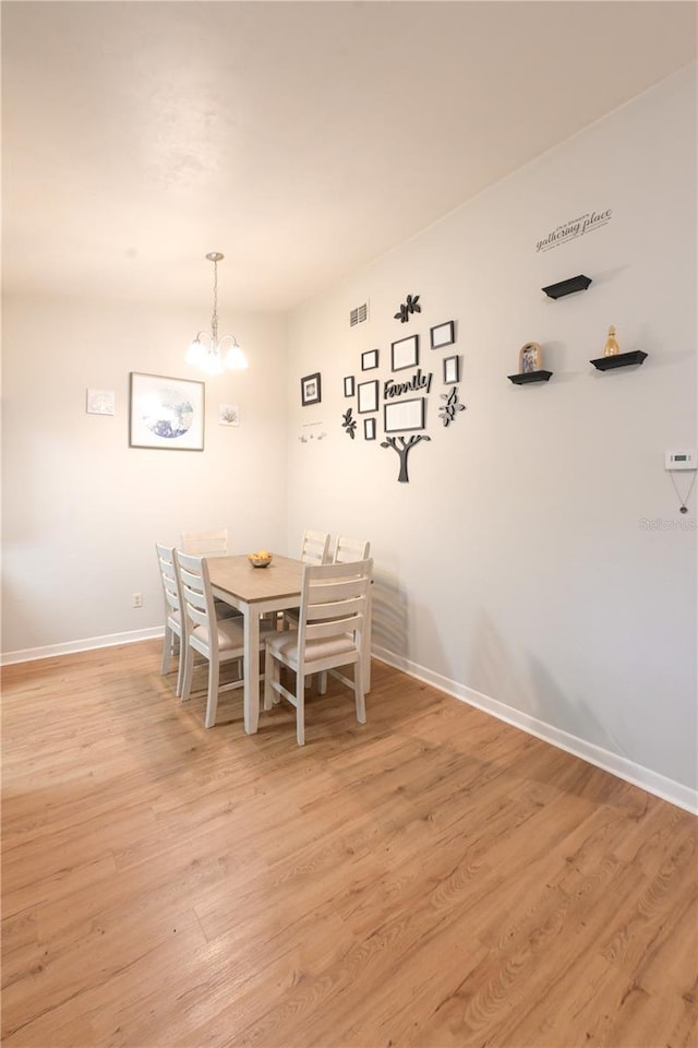 dining area with light wood-type flooring, baseboards, and an inviting chandelier