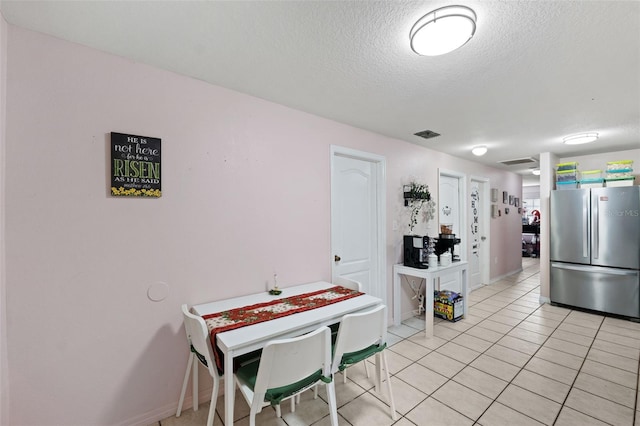 kitchen with stainless steel fridge, light tile patterned floors, and a textured ceiling