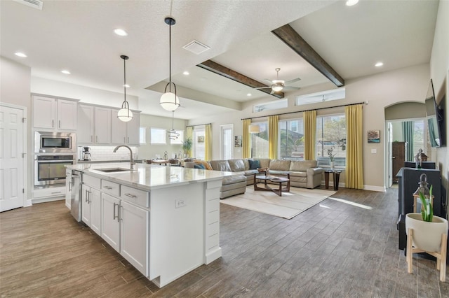 kitchen with appliances with stainless steel finishes, white cabinetry, an island with sink, sink, and beam ceiling