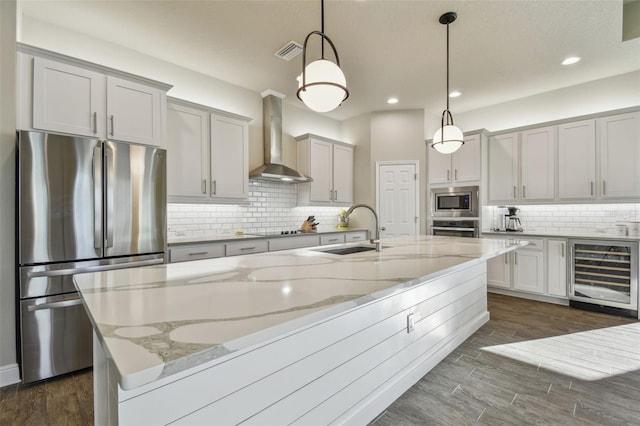 kitchen featuring pendant lighting, appliances with stainless steel finishes, beverage cooler, wall chimney range hood, and sink