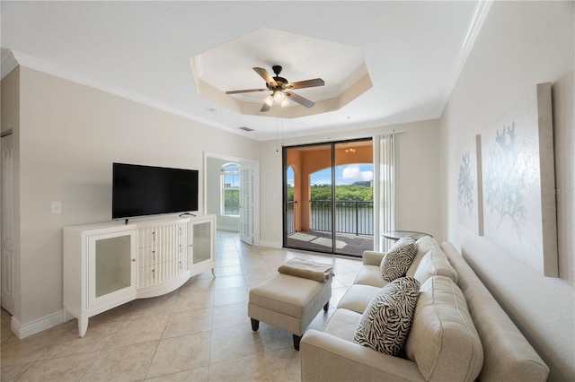 living room featuring ceiling fan, ornamental molding, light tile patterned floors, and a tray ceiling