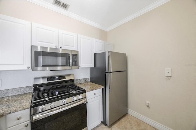 kitchen with stainless steel appliances, crown molding, light tile patterned floors, dark stone countertops, and white cabinetry