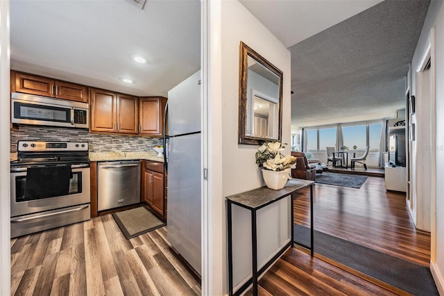 kitchen featuring appliances with stainless steel finishes, tasteful backsplash, light stone counters, and dark hardwood / wood-style floors