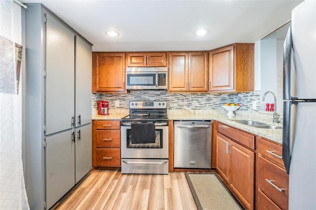 kitchen featuring light stone countertops, sink, light hardwood / wood-style floors, decorative backsplash, and appliances with stainless steel finishes